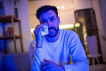 Man emotional and crying while watching TV alone.