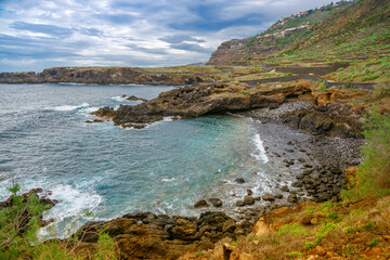 Dramatic rocky coastline of El Sauzal in Tenerife surrounded by lush greenery and calm waters