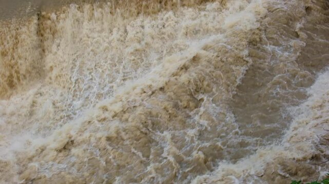 A full-flowing, large and rapid river with muddy water flows quickly. The water bubbles and foams. The river, muddy and overflowing after the rains, flows through the city.