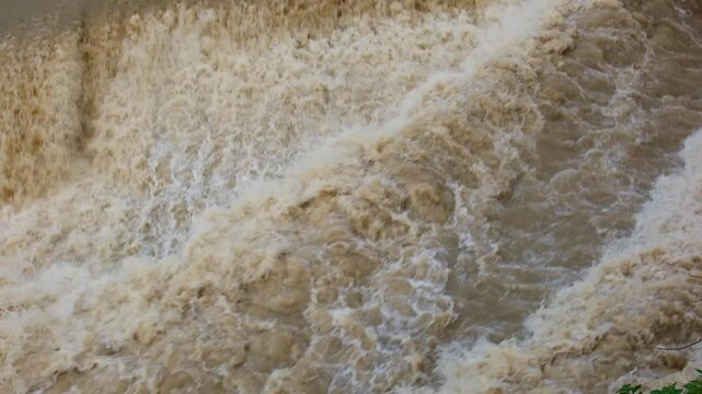 A full-flowing, large and rapid river with muddy water flows quickly. The water bubbles and foams. The river, muddy and overflowing after the rains, flows through the city.