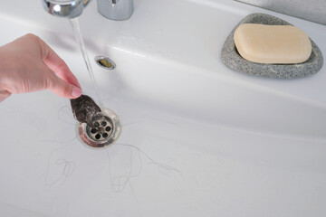 A lot of loose female hair in the sink. A woman removes garbage from the sink
