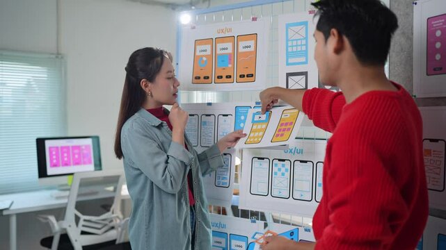 Professional ux designers collaborating on mobile app interface, analyzing sketches and discussing design improvements while strategizing user experience in modern startup office environment