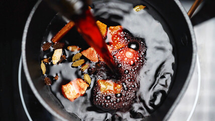 Pouring red wine into pot with fruits for mulled wine. Making of Mulled Wine.