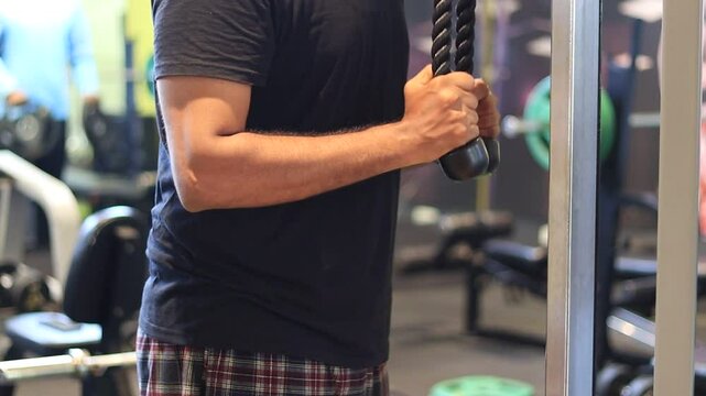 Tricep pushdown using rope exercise in a gym by a man wearing a black t-shirt to improve triceps. Tricep pushdown to build stronger arms