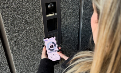 Young stylish woman getting access to the building by attaching smartphone to intercom. Concept of modern security technologies for access and smart home