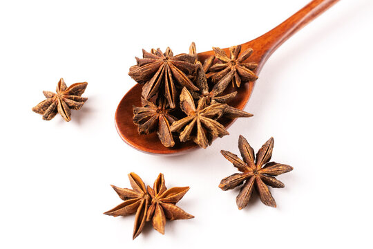 Star anise lies in a brown wooden spoon in close-up on a white isolated background.