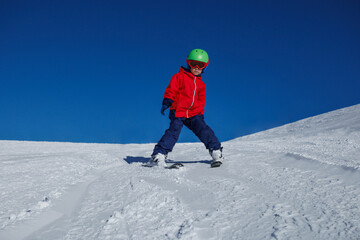 Child in red jacket makes a wide snowplows on gentle snowfield