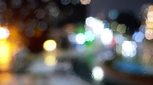 夜の雨に濡れた街を背景に窓越しに落ちる雨粒
