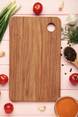 Cutting board, green onions, garlic, spices and tomatoes on pink wooden background. Cooking concept. Vertical photo