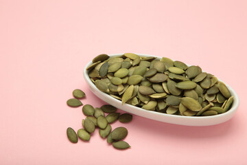 Pumpkin seeds in white plate on pink background.