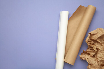 Rolls of white and brown baking paper on purple background