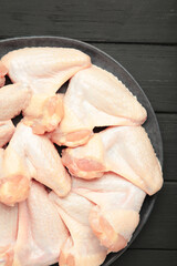 Raw chicken wings on dark plate on black wooden background. Vertical photo