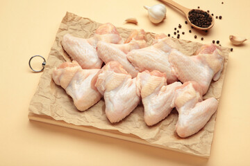 Raw chicken wings with ingredients for cooking on wooden cutting board on beige background.