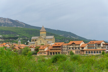 Fototapeta premium Mtskheta city. Svetitskhoveli Cathedral. Houses with beautiful balconies and orange tiled roofs. Mountains, hills and blue sky in the background