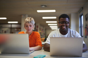 Smiling university students working on laptops in library