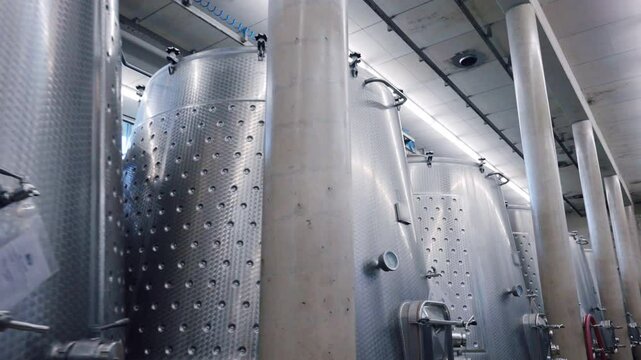 Stainless wine tanks for different production processes on factory, metal barrels with pipes and regulators, winemaking concept