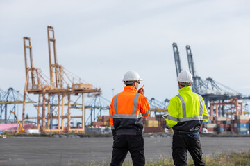Two port authority officers in high-visibility jackets and white helmets communicate via...