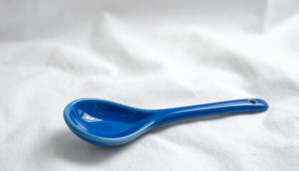 blue ceramic spoon rests elegantly on soft white fabric, showcasing its smooth surface and sleek design. This piece adds touch of color and style to any kitchen setting