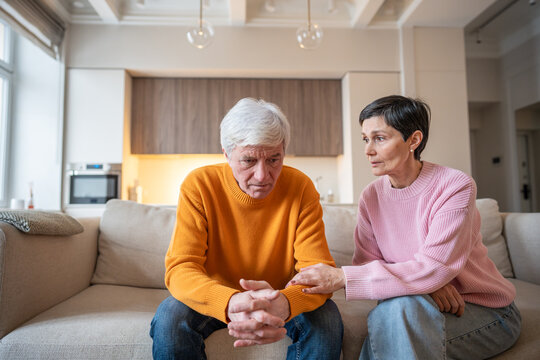 Worried wife supporting husband in emotional distress on sofa. Senior couple financial problems, work challenges and depression, difficult situation understanding, compassionate and consoling spouse