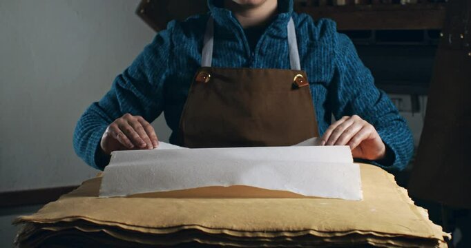 Super Slow Motion of Handmade Paper Sheet Being Carefully Handled on a Wooden Surface, Showcasing Its Texture, Deckled Edges, and Natural Imperfections in a Craft or Artistic Studio Environment.