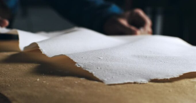 Super Slow Motion Close Up of Handmade Paper Sheet Being Carefully Handled on a Wooden Surface, Showcasing Its Texture, Deckled Edges and Natural Imperfections in Craft or Artistic Studio Environment.