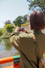 橋の上からスマートフォンで写真を撮る女性（タテ）