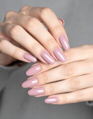 A close-up of a woman's hands featuring a glossy light pink manicure on neatly shaped and well-maintained nails.