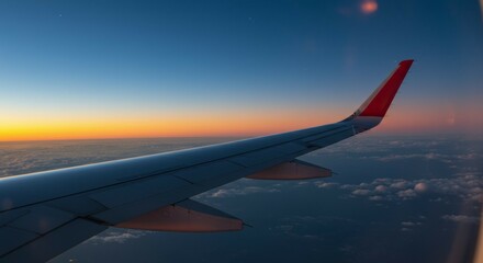 Fototapeta premium Airplane Wing View Above Clouds at Colorful Sunset