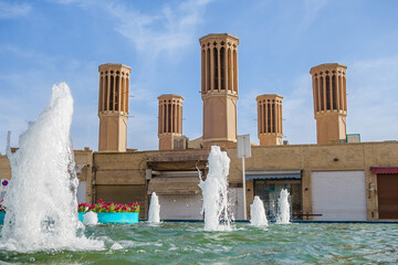 5 badgirs or wind towers, traditional cooling structures in the East. In the foreground is a city fountain with jets of water spewing out. Shot in Amir Chakhmaq Square in Yazd, Iran