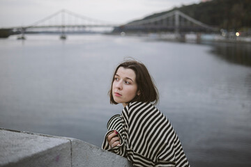 Fototapeta premium Pensive young woman near the river on the background of the city river.