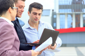 Business meeting outdoors. Two men and one woman are discussing a new project in the background of...