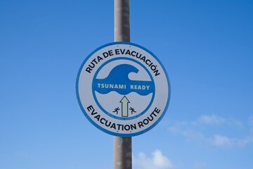 Multilingual tsunami warning sign marking safe evacuation path, guiding coastal residents toward...