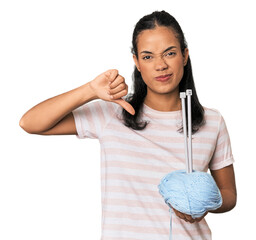 Young Filipina holding yarn showing a dislike gesture, thumbs down. Disagreement concept.