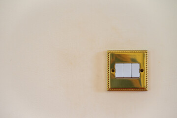 Triple light switch. Gold switch with white details and magnolia wall. All switches in off position. No branding. Copy space to left.