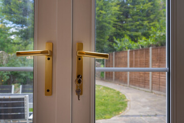 Detail of patio doors with garden beyond. Gold handles with key inserted into lock.