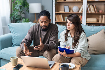 Young intelligent innovative couple presenting their startup new business idea via video call on laptop computer, sitting at home on sofa, talking to potential investor. Technology innovation.