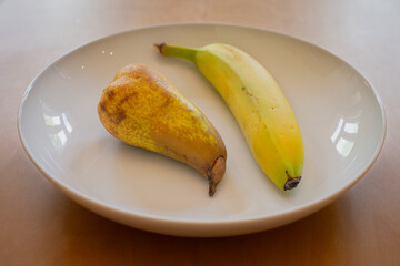 One pear and one banana in a white dish on a wooden table