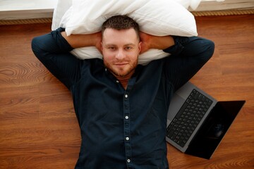 Fototapeta premium Relaxing man relaxing with laptop nearby. Man lying comfortably on the floor with a pillow, enjoying a quiet moment next to his laptop in the middle of natural light.