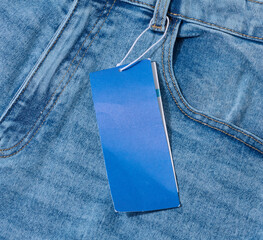 Close-up of light blue denim jeans with a blank blue price tag attached to the belt loop.