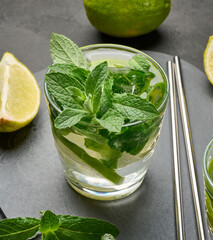 Glass of mojito cocktail with fresh mint leaves, lime slices, and ice cubes on a dark stone background.