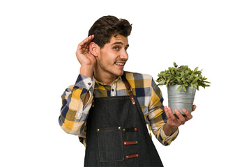Young caucasian gardener man isolated on white background trying to listening a gossip.