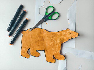 Bear figure cut out with scissors on white table. Children's creativity.