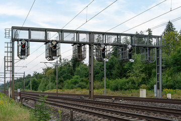 Railway line with signal bridge. Signals hanging from signal bridge, showing red and orange lights....