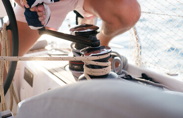 Man working on sailing yacht ropes and winch. Sailboat equipment details. Water transport, marine...