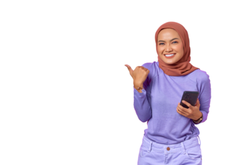 Smiling Asian woman holding a mobile phone while pointing a thumb at copy space isolated on transparent background