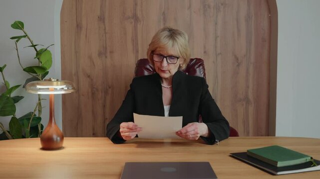 A 60-year-old blonde woman, working remotely as a senior business specialist, tears up a printed report in frustration after spotting incorrect data. Her reaction shows high expectations.