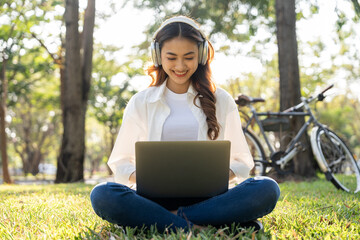 Young asian teenager learning with laptop sitting in the public park. Summer time spring young...