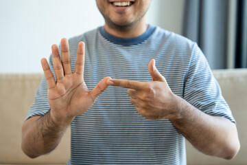Portrait view of happy young deaf asian man showing sign language and looking at camera at home, a...