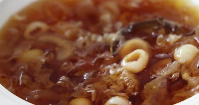 Hand held shake video of Traditional Chinese sweet soup dessert made of longan fruit sugar snow fungus red dates in white dish being served 