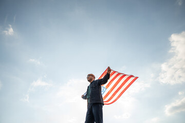 Portrait of cheerful young man looking forward while standing proudly with holding USA flag over...